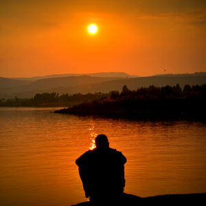 a silouhette of person facing a lake in the evening